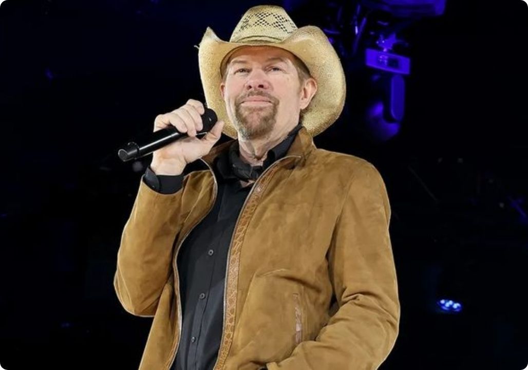 ““An old soldier stood up. And the entire hall held its breath.” – The moment Toby Keith left America in silence That night was supposed to belong to Toby Keith. The blazing lights, the roaring guitars, thousands of voices shouting his name. But all of it suddenly meant nothing when Toby stopped singing. In the front row, a 93-year-old man quietly leaned on his cane. No introduction. No name on a screen. No spotlight. Just a World War veteran — a man who once walked through battlefields and then quietly stepped out of history.”